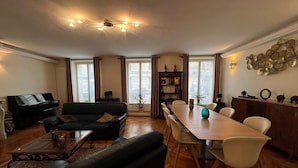 A living room with a piano, sofa, coffee table, dining table with chairs, and a bookshelf. - In the Heart of Paris - Spacious 153 m² (Paris)