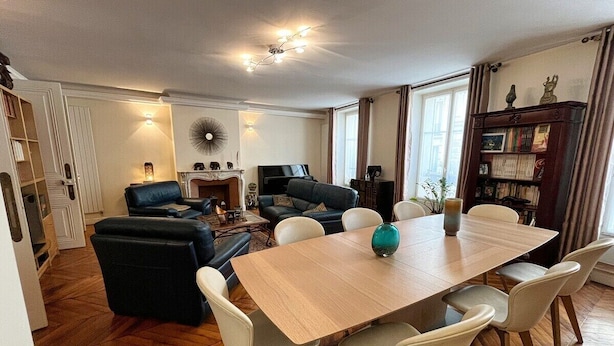 A spacious living area with a wooden dining table, comfortable seating, a fireplace, and a bookshelf. - In the Heart of Paris - Spacious 153 m² (Paris)