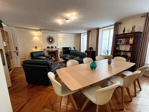 A spacious living area with a wooden dining table, comfortable seating, a fireplace, and a bookshelf.