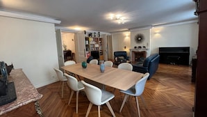 A dining area with a wooden table and white chairs, a sofa, and a television in a living room. - In the Heart of Paris - Spacious 153 m² (Paris)