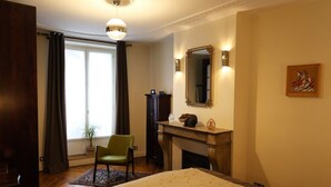 A bedroom with a bed, a chair, a fireplace, and a large window with curtains. - In the Heart of Paris - Spacious 153 m² (Paris)
