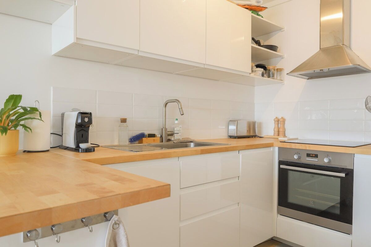 Une cuisine moderne avec des armoires blanches, une hotte en acier inoxydable, un four encastré et un plan de travail en bois.
