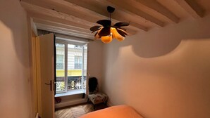 Un dormitorio con cama, ventana, silla y ventilador de techo.