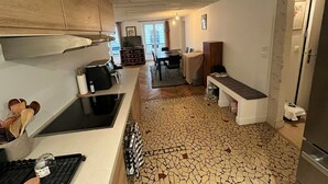 Una cocina compacta con suelo de baldosas, armarios de madera, una banca y una zona de comedor al fondo.