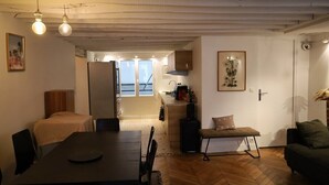 Una sala de estar acogedora con una mesa de comedor, un sofá y un banco. Hay una zona de cocina con armarios y un refrigerador.