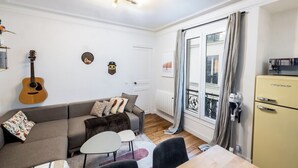 Una sala de estar con un sofá, una mesita, una guitarra y un refrigerador.