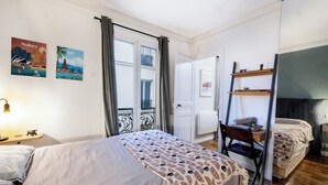Un dormitorio con cama, escritorio y silla. Hay dos carteles en la pared, uno de Sydney y otro de Bali.