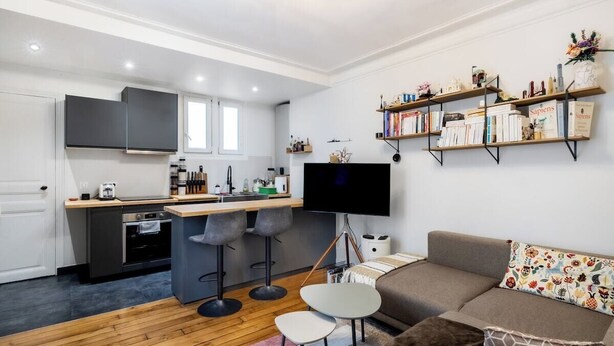 Un apartamento moderno con cocina, comedor y sala de estar. Cuenta con un televisor de pantalla plana, un sofá y una estantería.