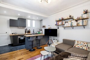 A modern apartment with a kitchen, dining area, and living room. It includes a flat-screen TV, a sofa, and a bookshelf. - Paris 17 - Charming 2-room in Batignolles (Paris)