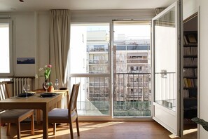 A dining area with a table set for two, a chair, a potted plant, and a bookshelf.