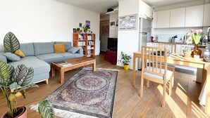 A modern living room with a sofa, coffee table, and a dining area with a table and chairs. There is a bookshelf and a TV in the background. - Garden View Apartment near Canal Saint-Martin (Paris)