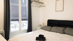 Une chambre d’hôtel dotée d’une grande fenêtre, d’un lit recouvert d’une couette blanche, d’une tête de lit noire et d’oreillers gris portant le nom de la marque « LESTRA ».