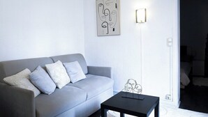 Un salon moderne avec un canapé gris, des coussins blancs, une table basse noire et une œuvre d'art abstraite accrochée au mur.