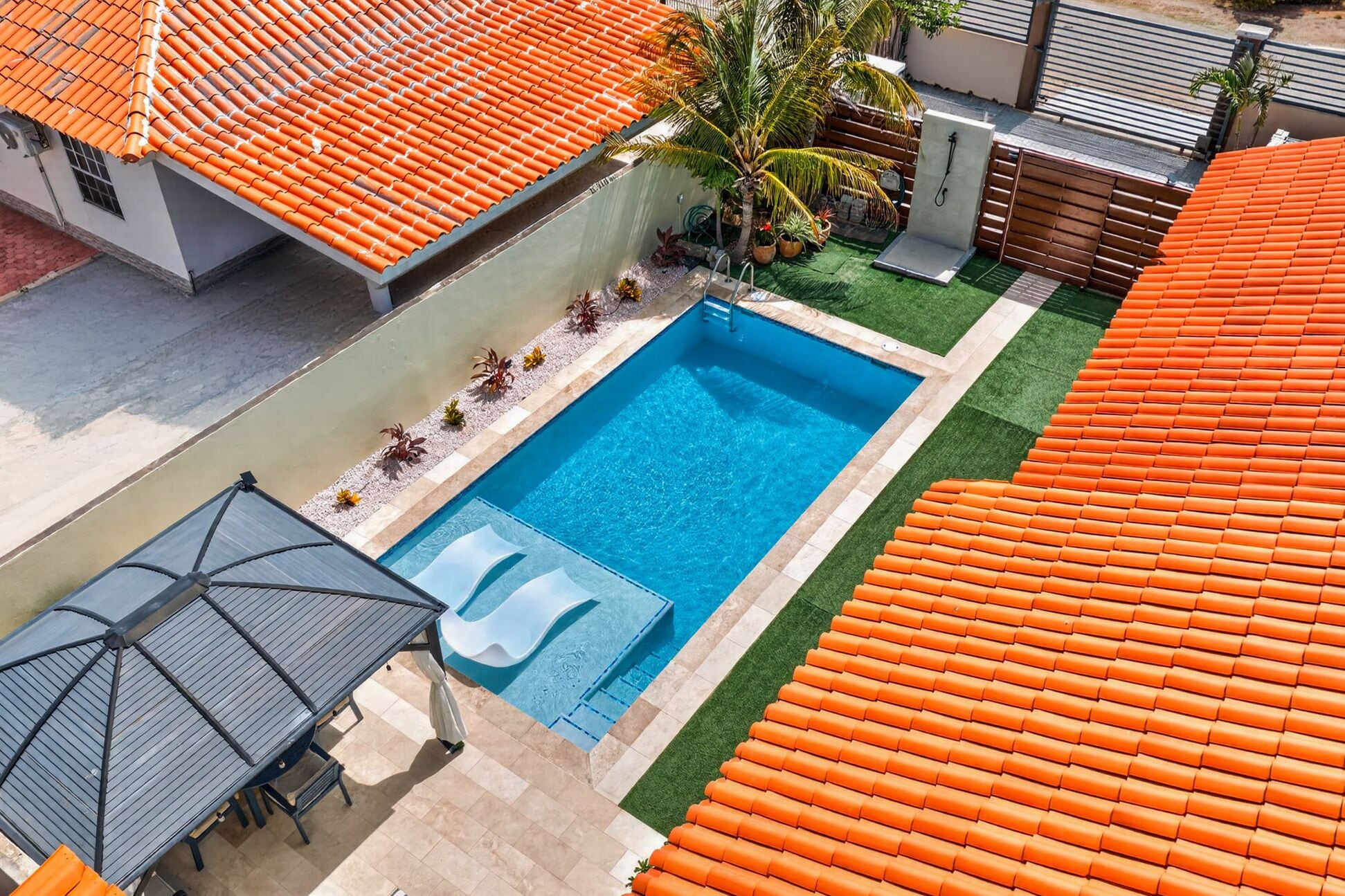 Ein Dachpool mit Rutsche, umgeben von einer Terrasse mit orangefarbenen Fliesen und einer Palme.