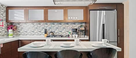 A modern kitchen with wooden cabinets, a stainless steel refrigerator, and a central island with black chairs.