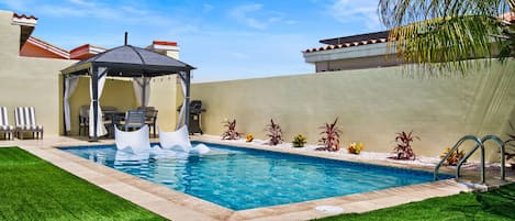 A swimming pool with a gazebo, lounge chairs, and a palm tree.