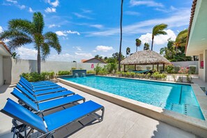 Une piscine bordée de chaises longues bleues, une structure à toit de chaume et des palmiers.