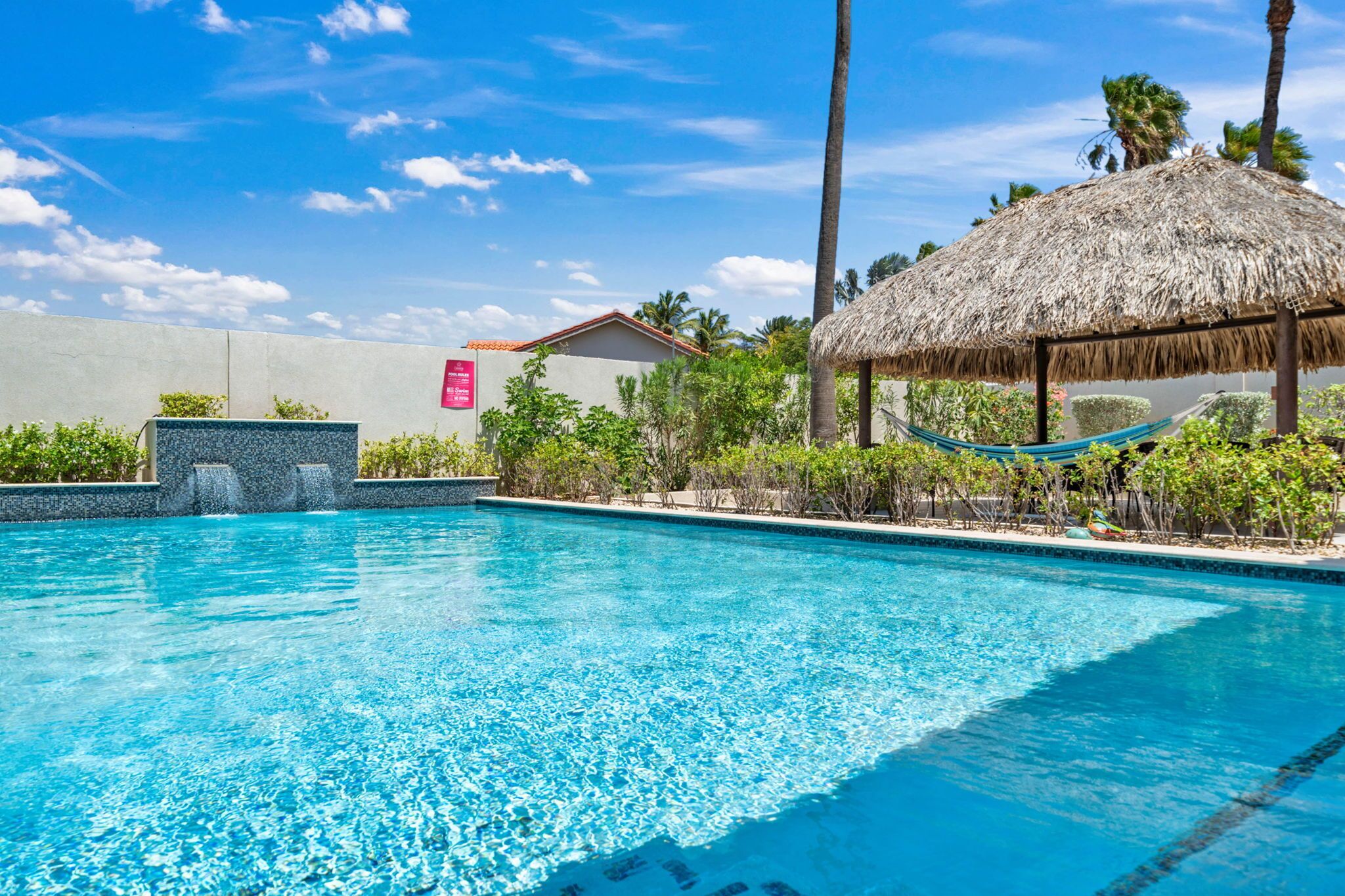 Una piscina azul cristalina con una estructura de techo de paja y una hamaca.