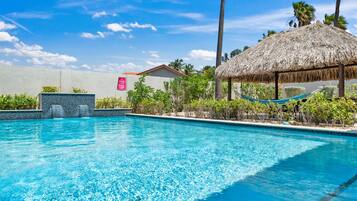 Una piscina azul cristalina con una estructura de techo de paja y una hamaca.