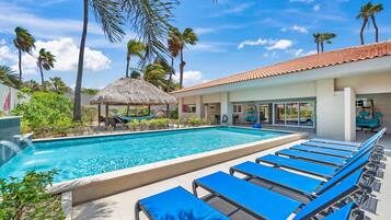 Una piscina con sillas de descanso, una estructura de techo de paja y palmeras.