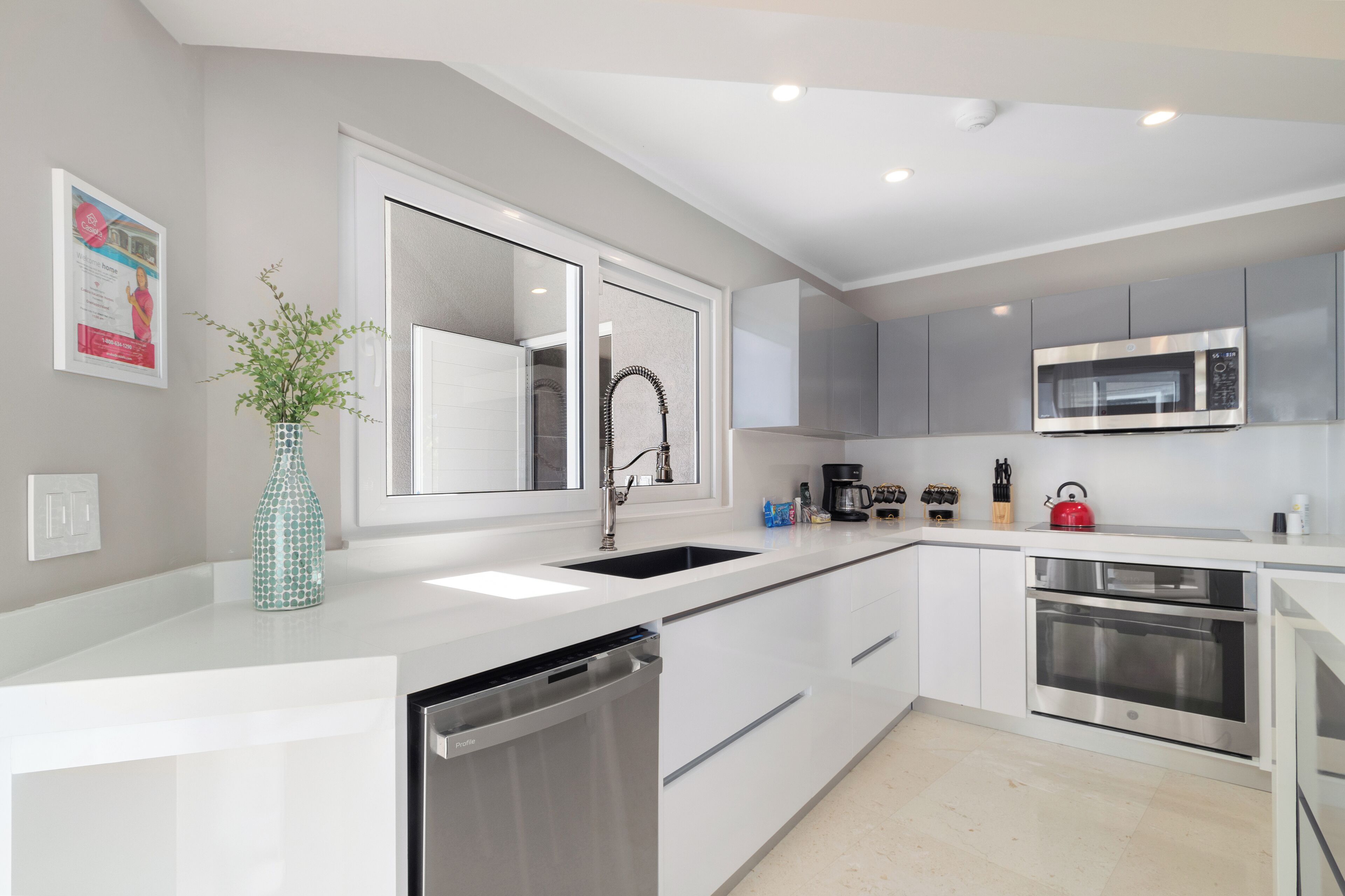 A modern kitchen with white cabinets, a stainless steel sink, a microwave, and an oven.