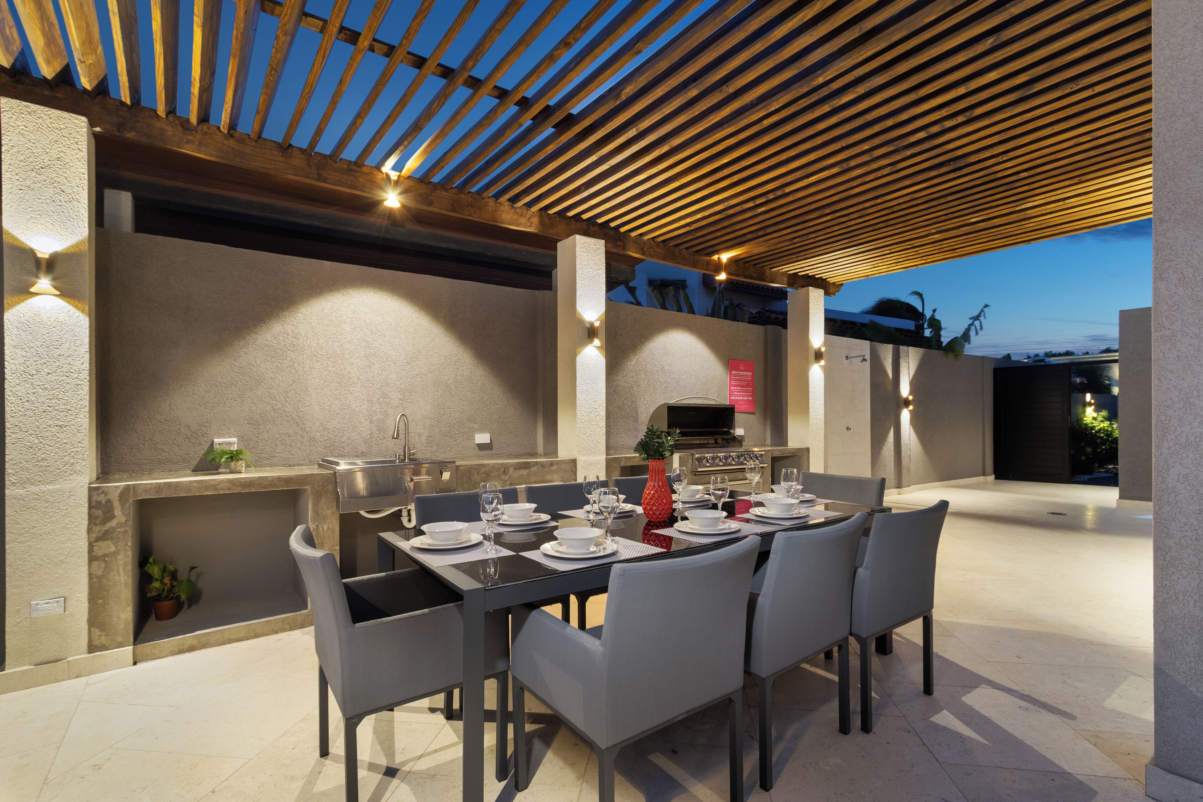 An outdoor dining area with a pergola, a built-in grill, and a seating arrangement.