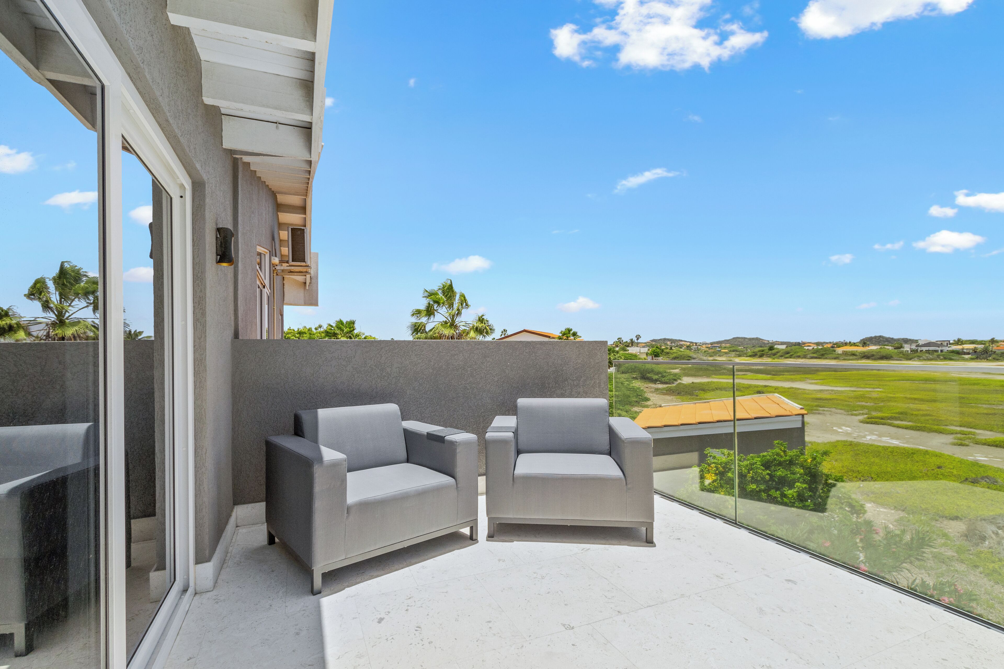 Un balcon avec deux fauteuils gris et une porte vitrée donnant sur un espace patio.