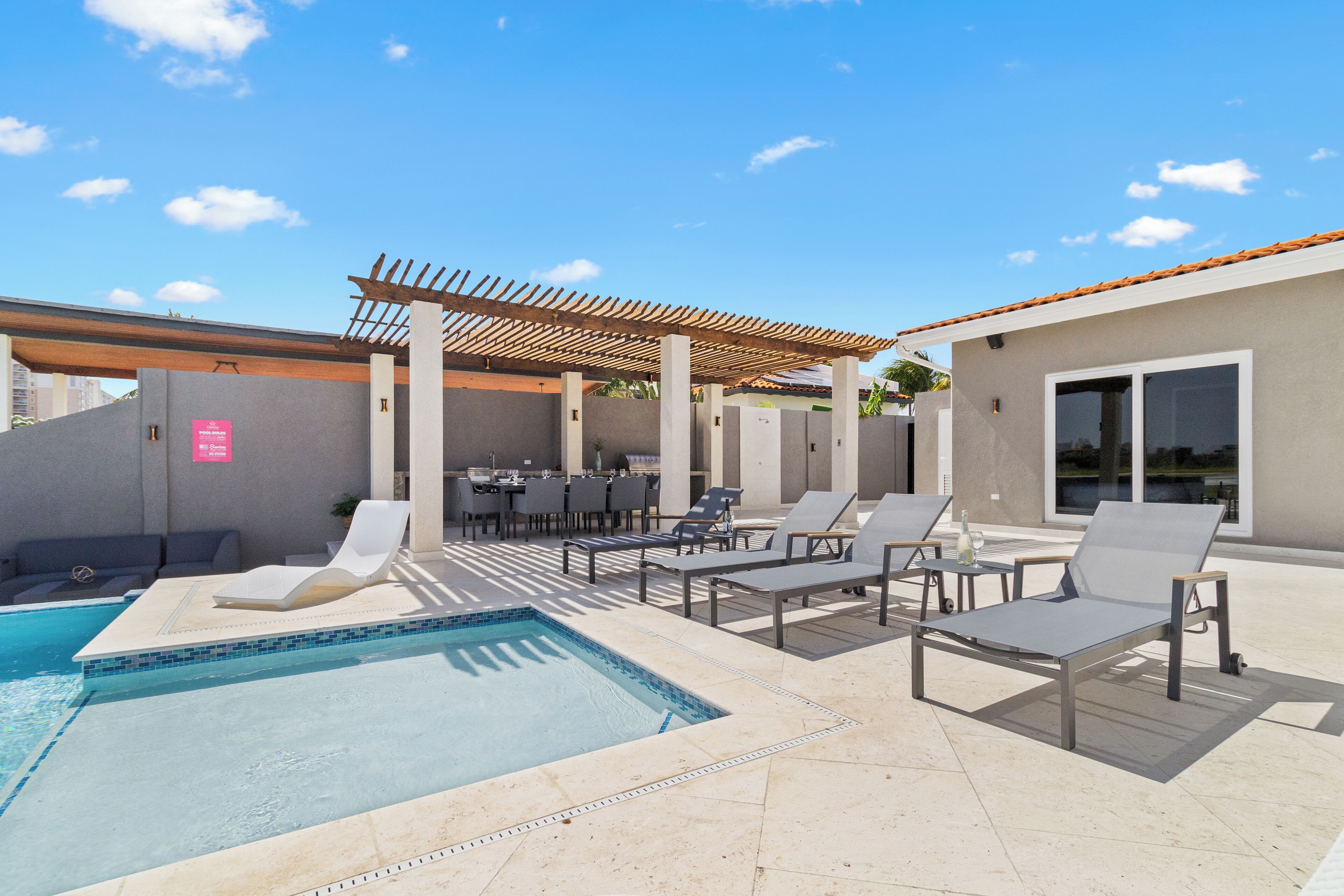 Un área junto a la piscina con sillones de descanso, una pérgola y una zona de comedor.