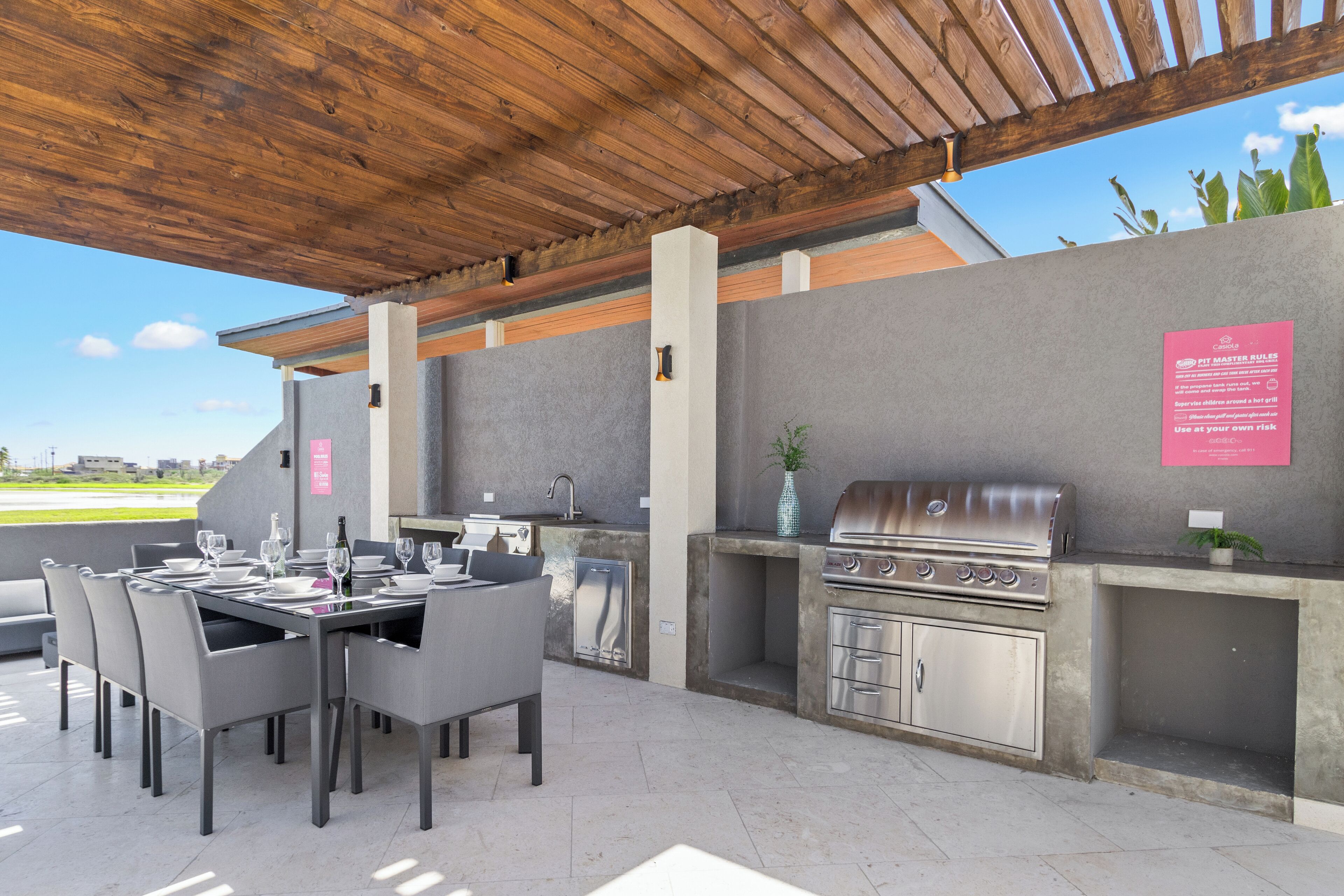 Un patio al aire libre con una mesa de comedor preparada para cuatro personas, una parrilla y un lavamanos.
