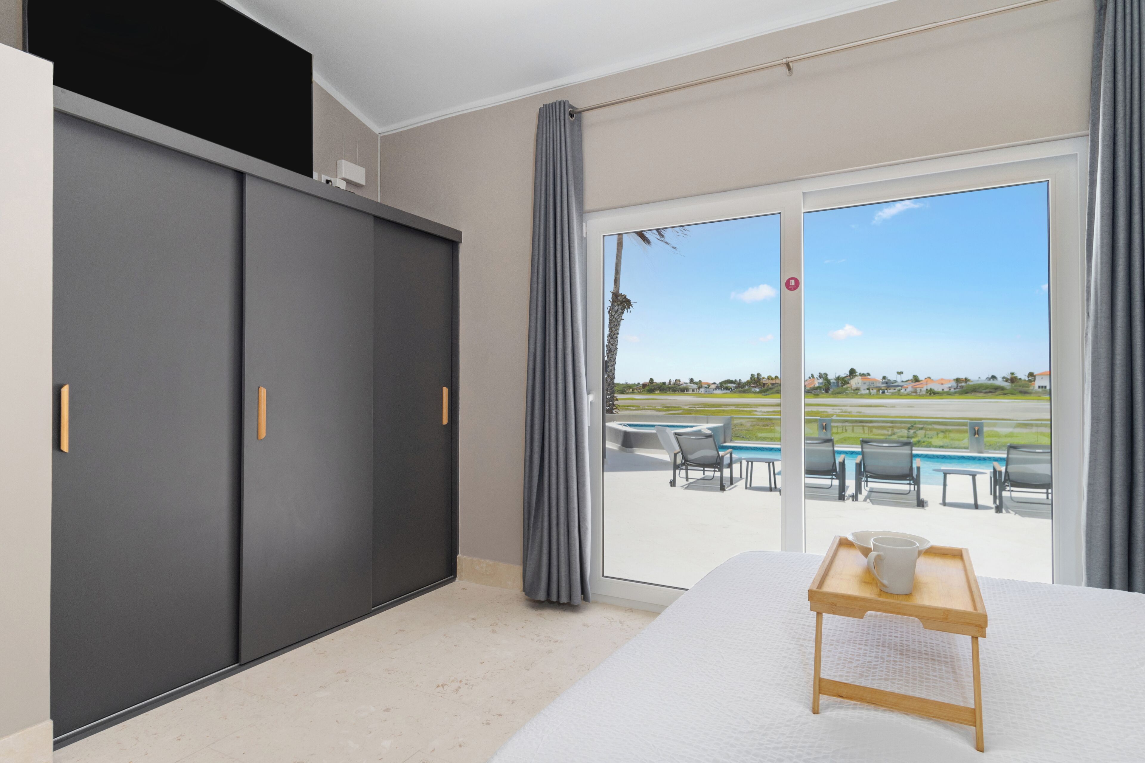 Habitación de hotel con una cama grande, puerta corrediza a un balcón y vista a una piscina y mobiliario exterior.