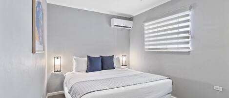 Un dormitorio con cama, ventilador de techo, unidad de aire acondicionado y ventana con persianas.