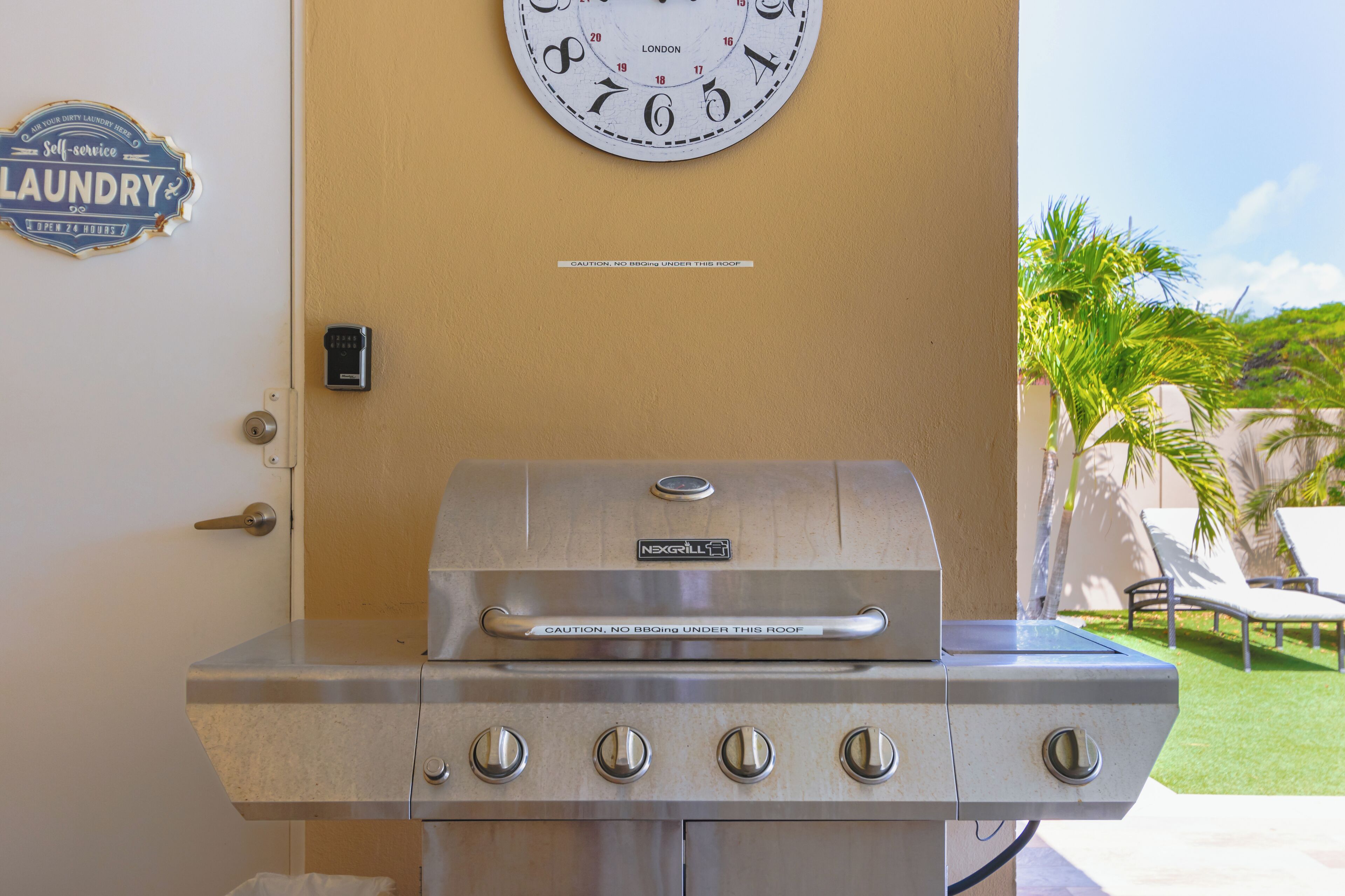 A stainless steel outdoor grill with a caution sign, a wall clock, and a laundry sign.