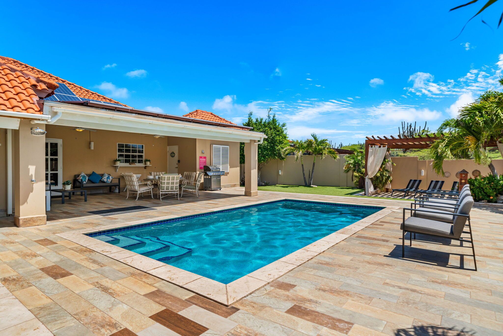 Un giardino con piscina, mobili da patio e una zona relax coperta.