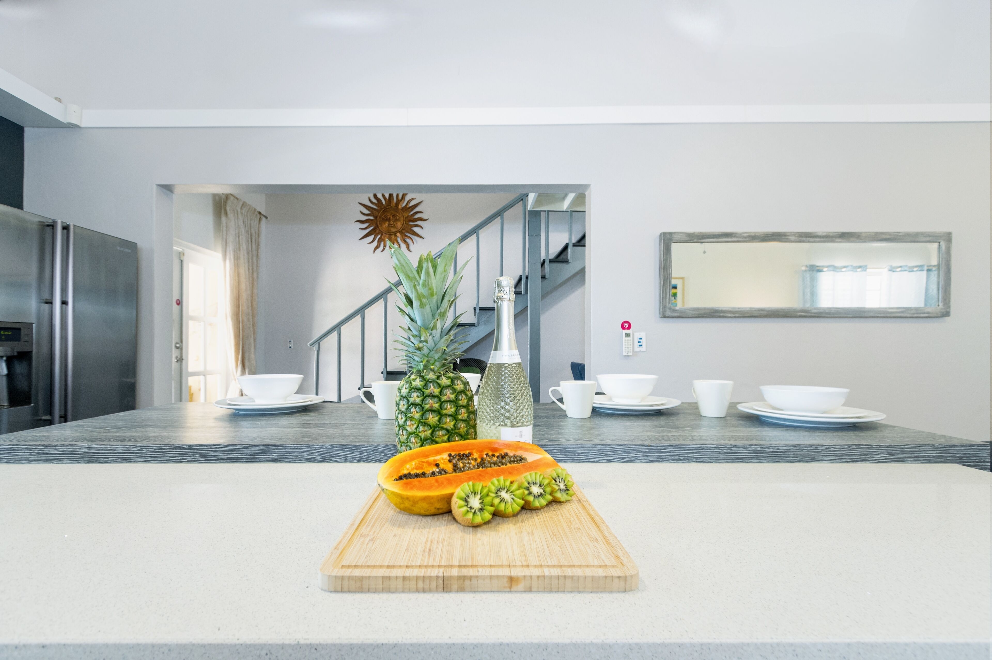 Eine moderne Küche mit einem Holzer Schneidebrett, auf dem eine Ananas, eine Flasche und eine Schüssel mit Obst liegen.