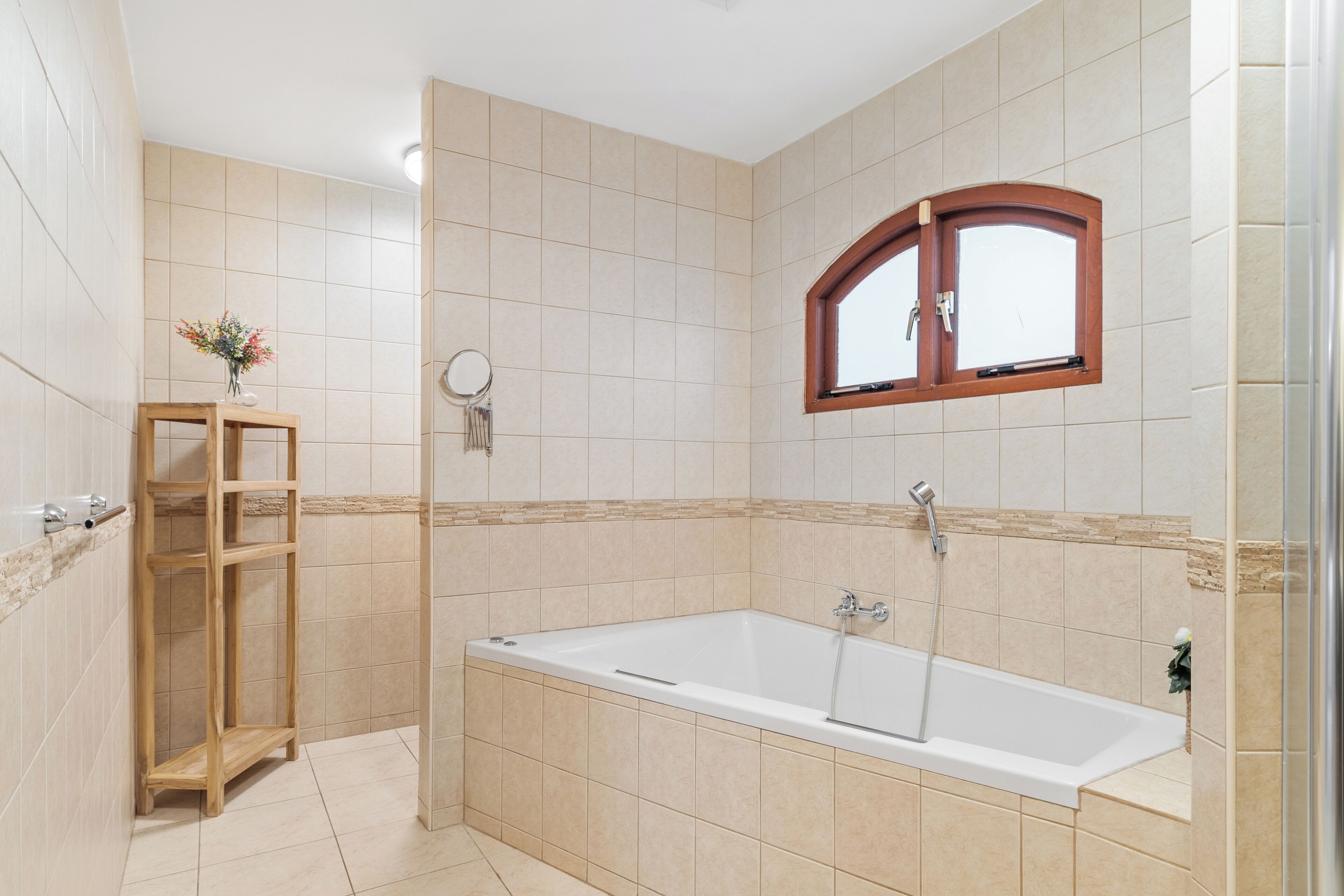 A modern bathroom with a bathtub, a wooden shelf, and a window.