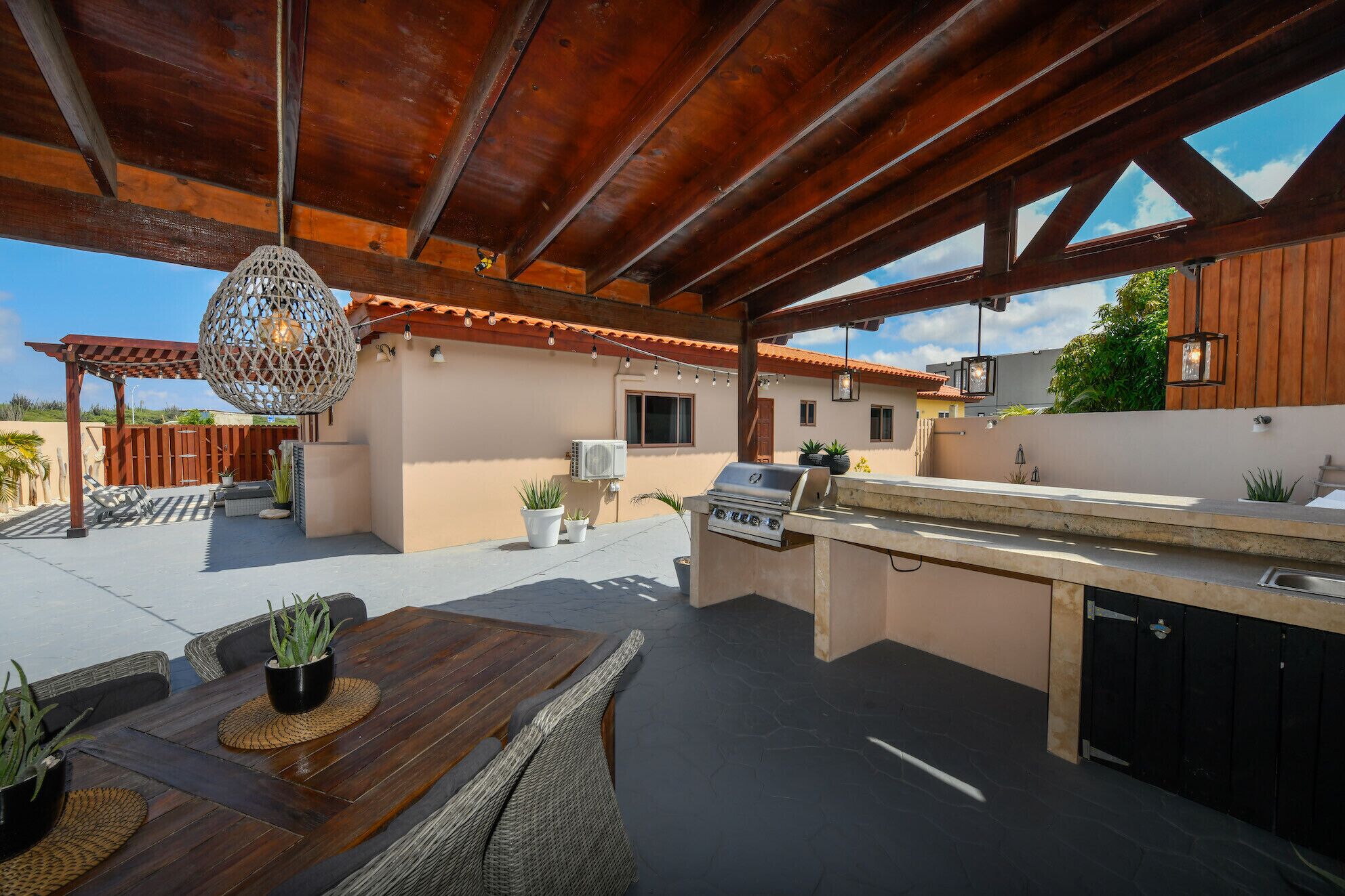 Eine Terrass mit Holz-Pergola, einer hängenden Lampe, einem Grill und Kübelpflanzen.