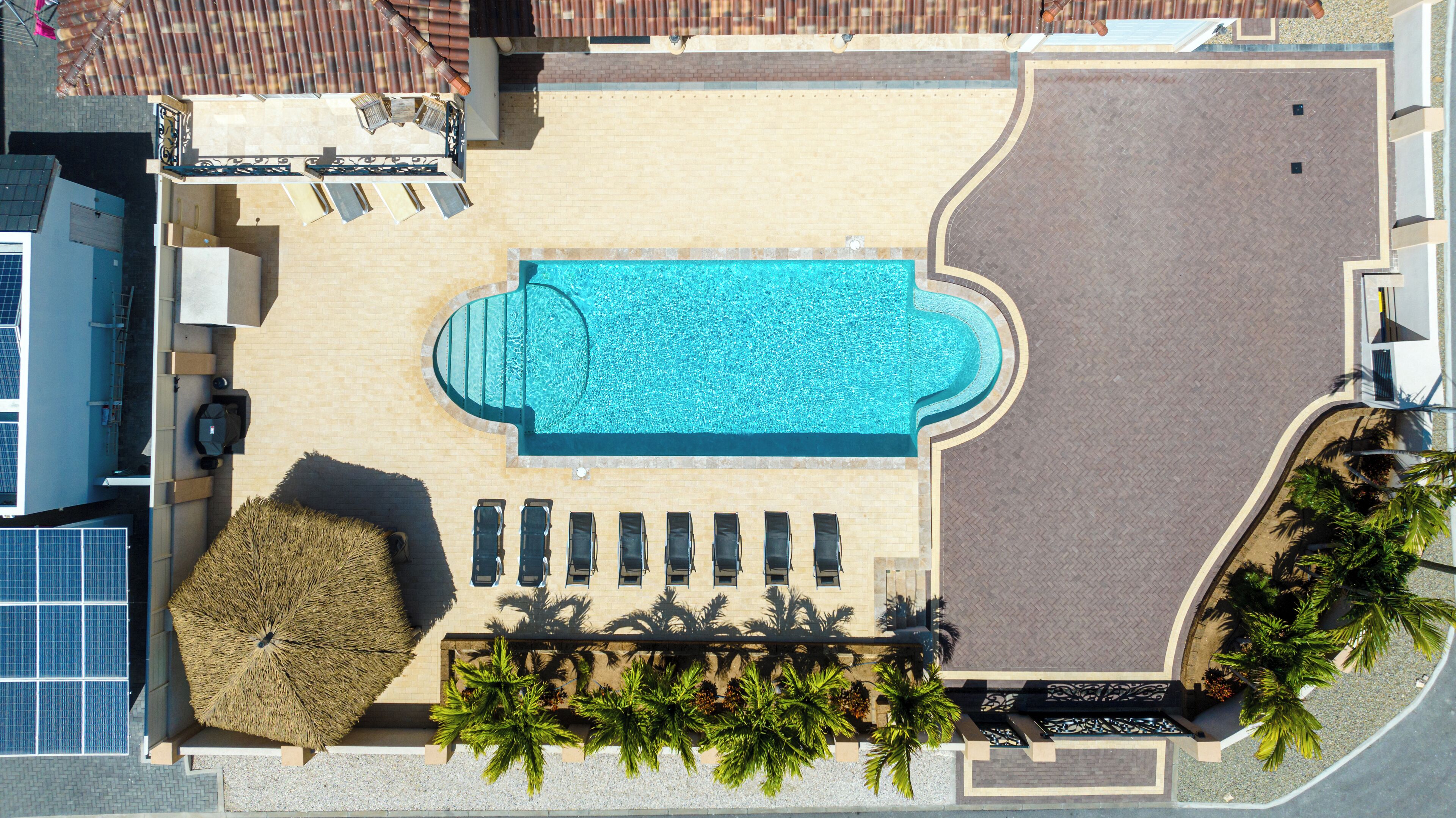 Vue aérienne d’un hôtel avec une piscine, des chaises longues, un parasol en chaume et des palmiers.