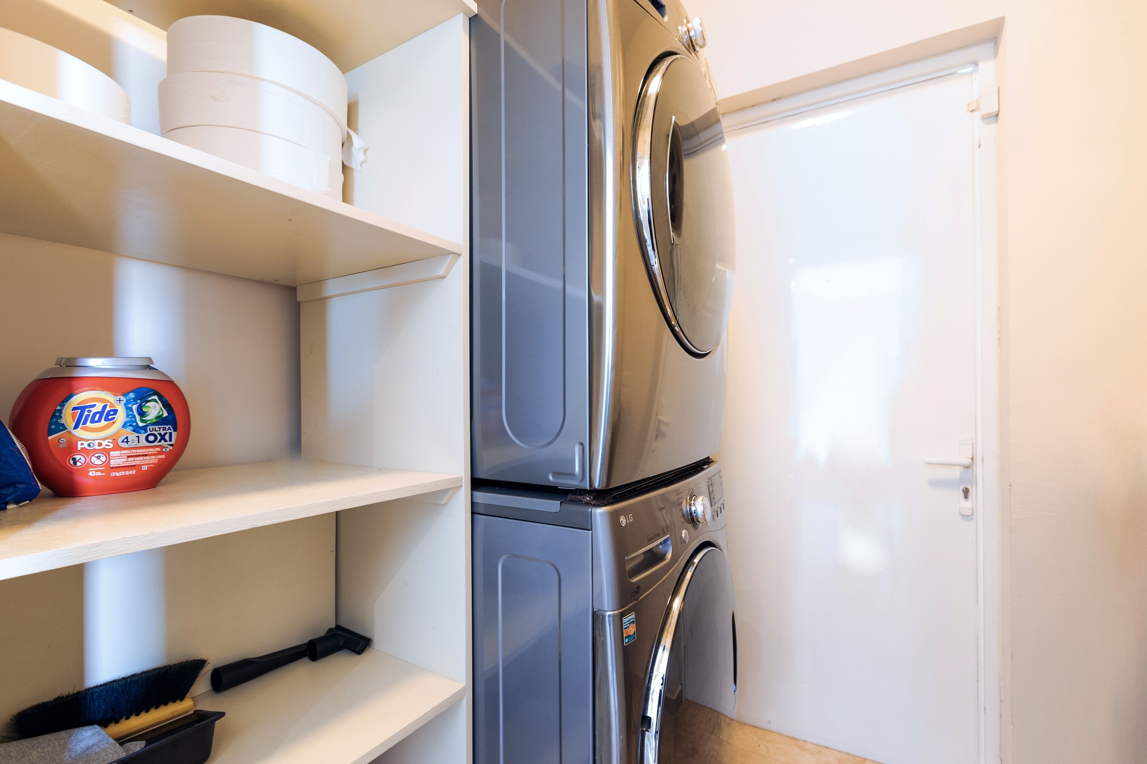 A compact laundry area with a washing machine and dryer, a shelf with cleaning supplies, and a white door.