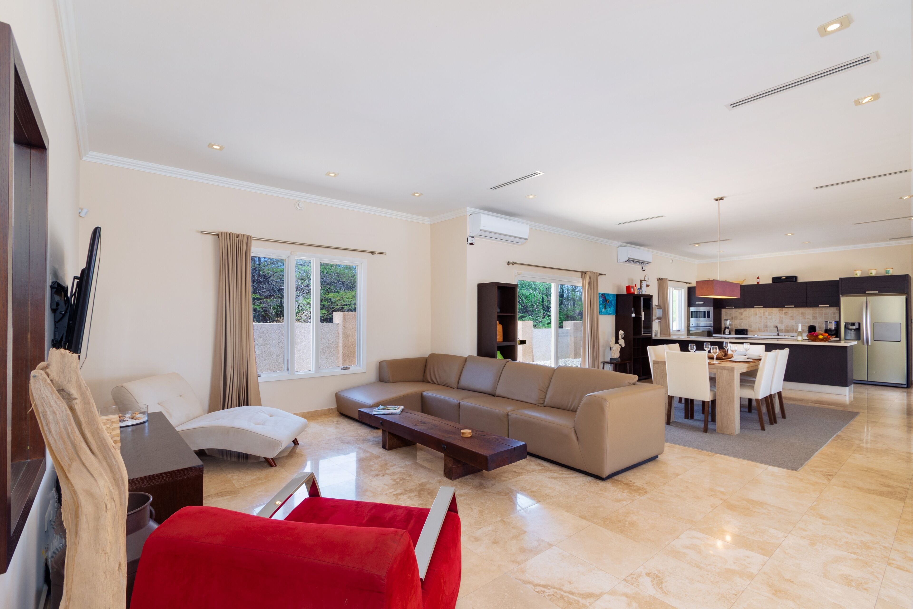 A spacious living room with a large sofa, a red chair, and a dining area with a table and chairs.