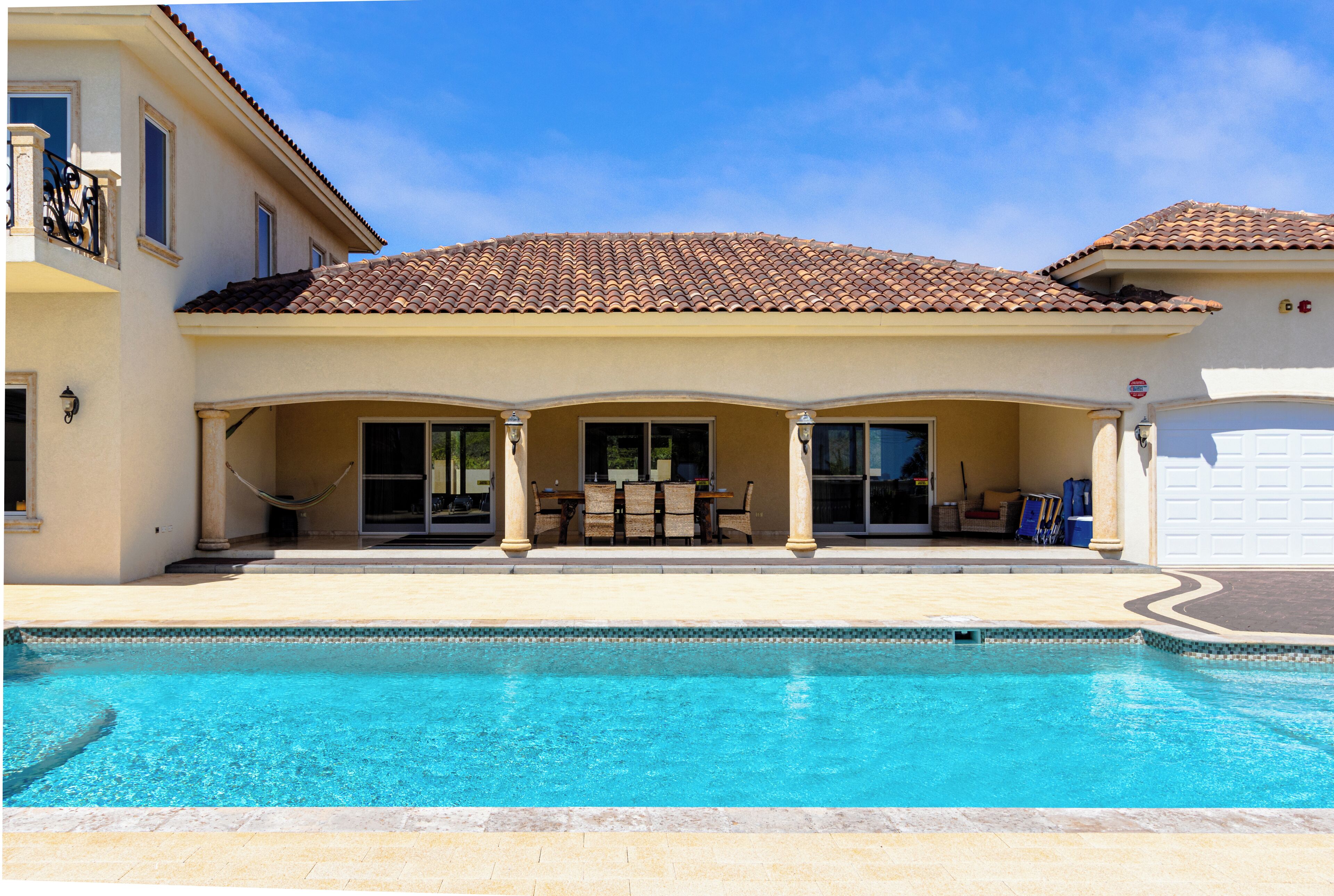 A two-story house with a swimming pool, a covered patio with outdoor furniture, and a garage.