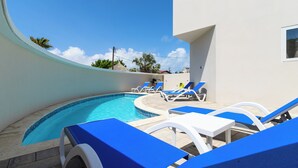 Una piscina con sedie a sdraio blu e un edificio bianco sullo sfondo.