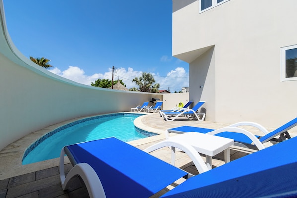 A swimming pool with blue lounge chairs and a white building in the background.