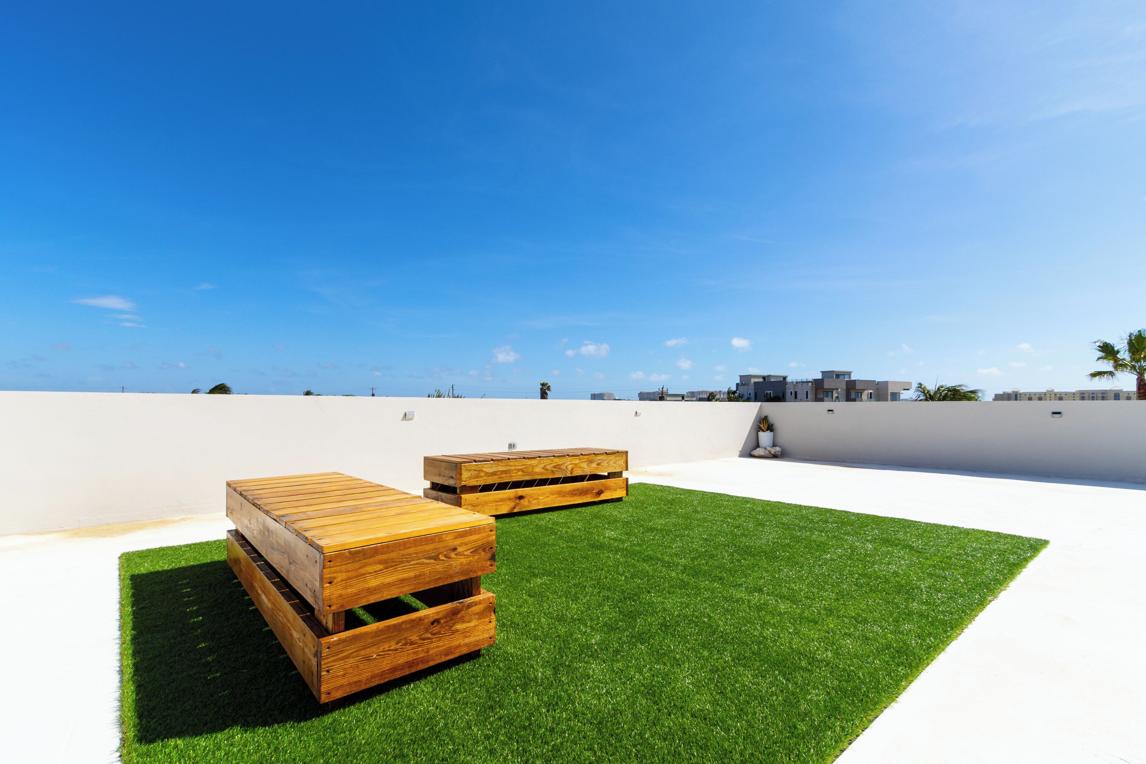 A rooftop terrace with two wooden benches and a white wall in the background.