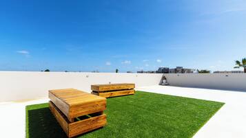 Una terraza en la azotea con dos bancos de madera y un muro blanco al fondo.