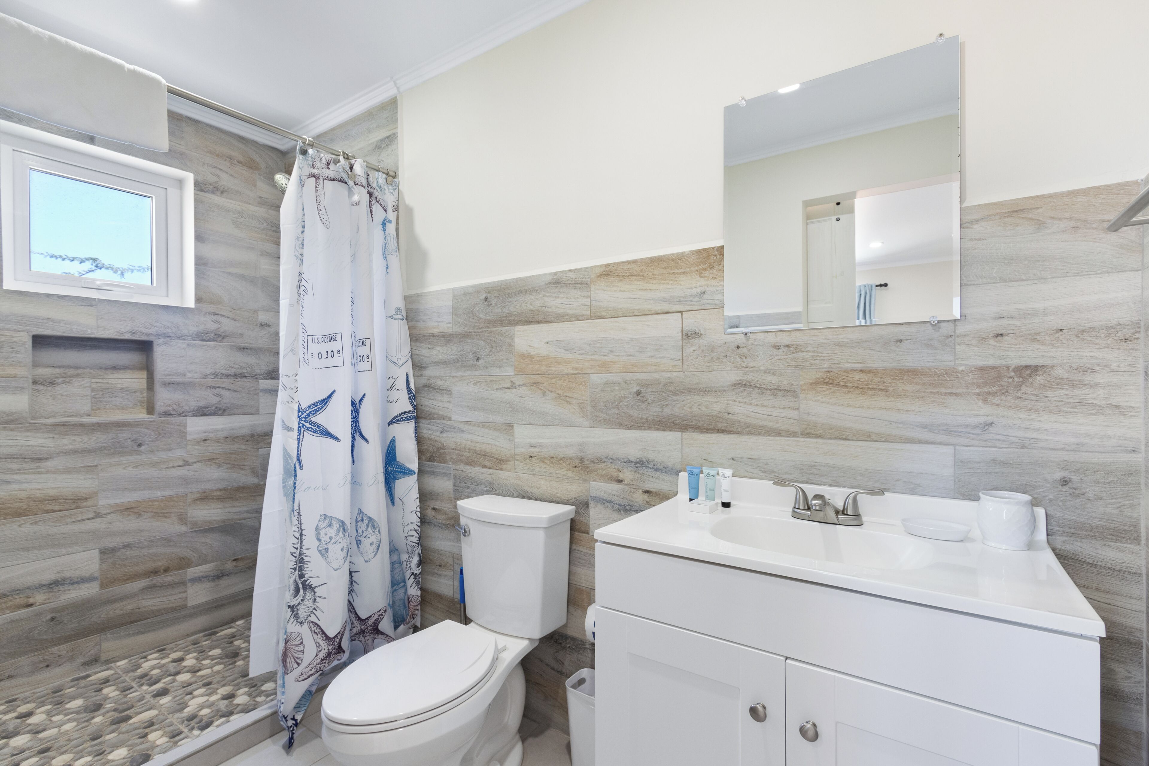 A bathroom with a shower curtain, toilet, sink, and mirror.