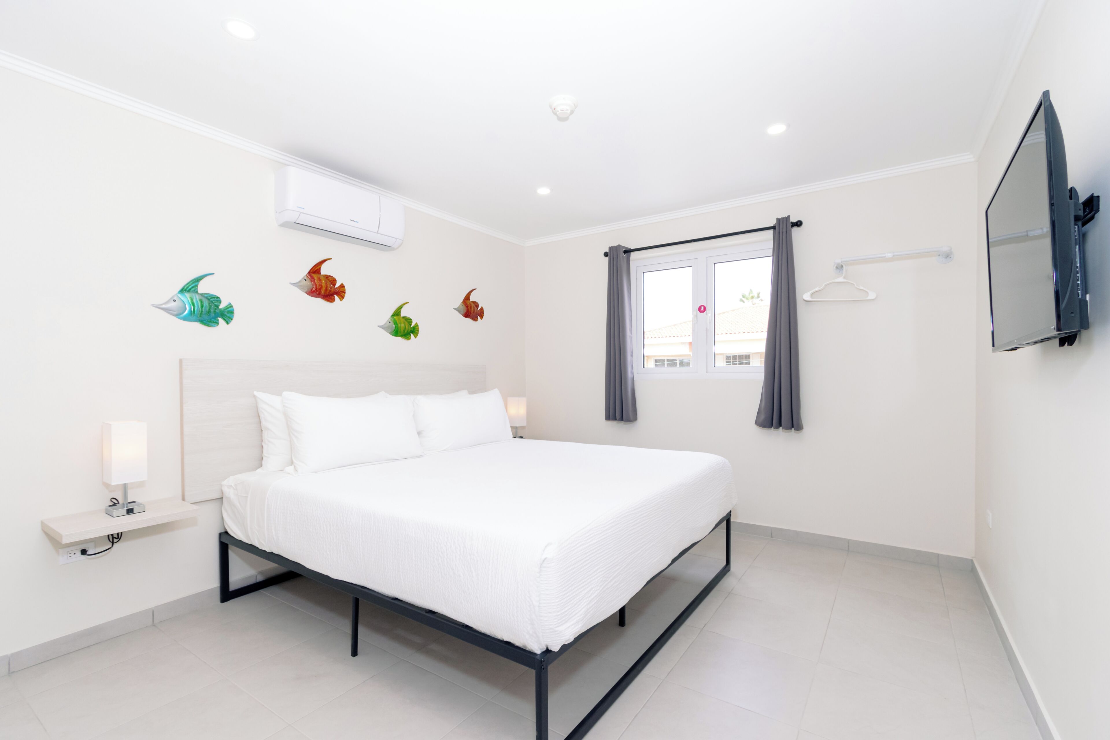 A modern hotel room with a large bed, a flat-screen TV, a bedside table with a lamp, and decorative fish wall decals.