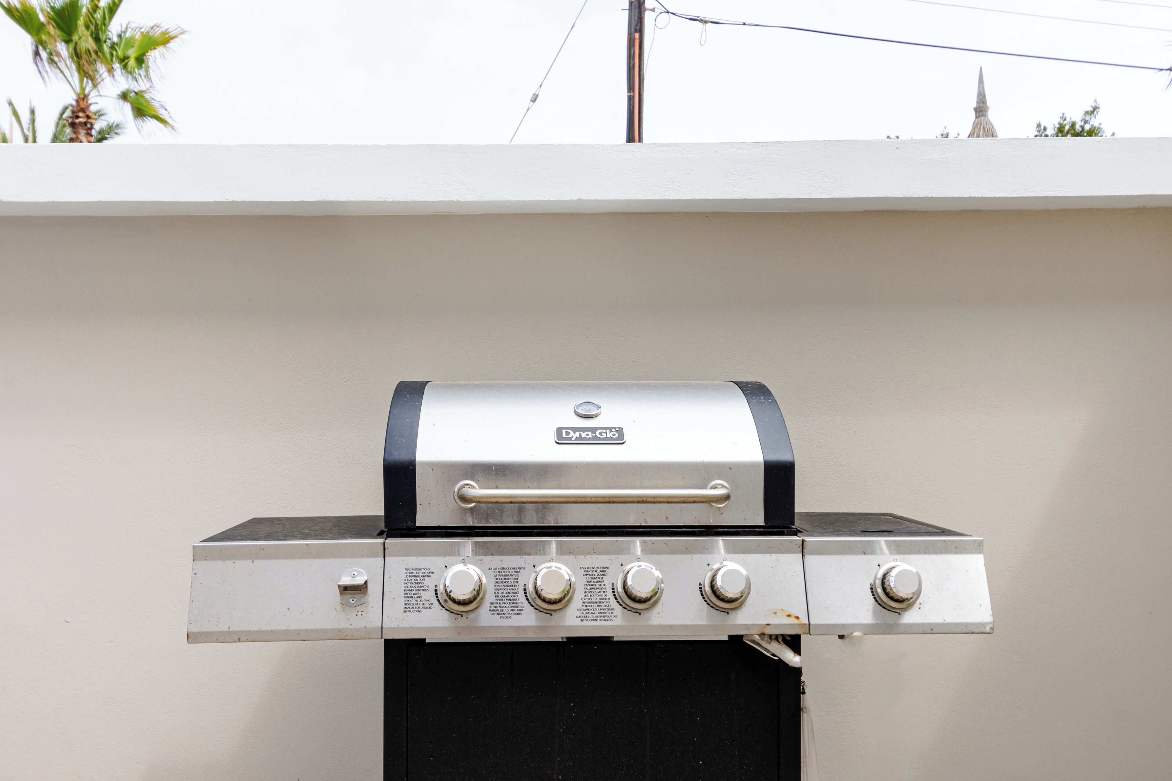 A gas grill with four burners and a control panel, mounted on a white wall.