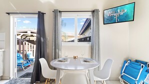 A dining area with a round table, two chairs, and a TV on the wall.