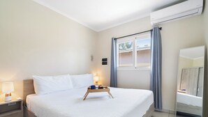 A neatly made bed with a tray of items, a bedside lamp, and a window with curtains.