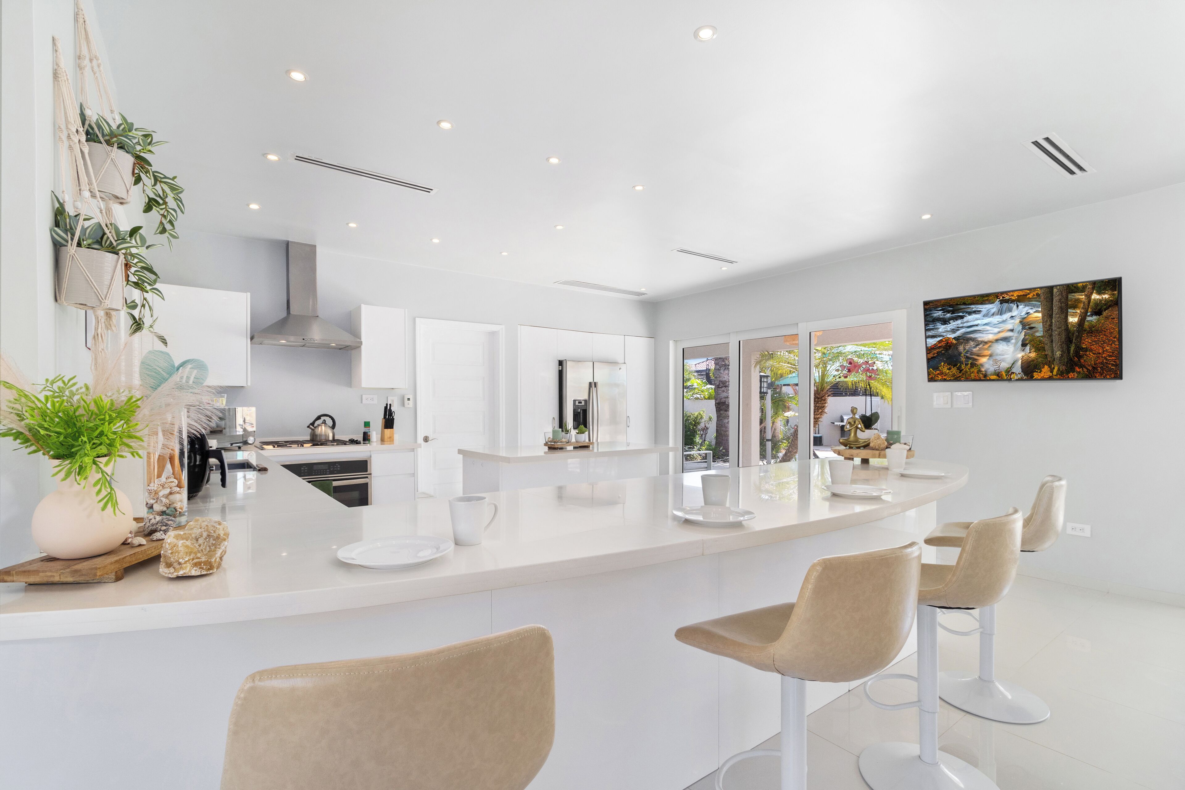 Una cocina moderna con armarios blancos, una isla central con taburetes y un amplio ventanal con vistas al exterior.